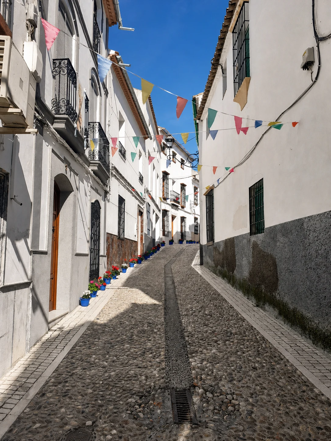 Fotografía real de una calle en pendiente de Castro del Río, con fachadas blancas, balcones, banderines y macetas